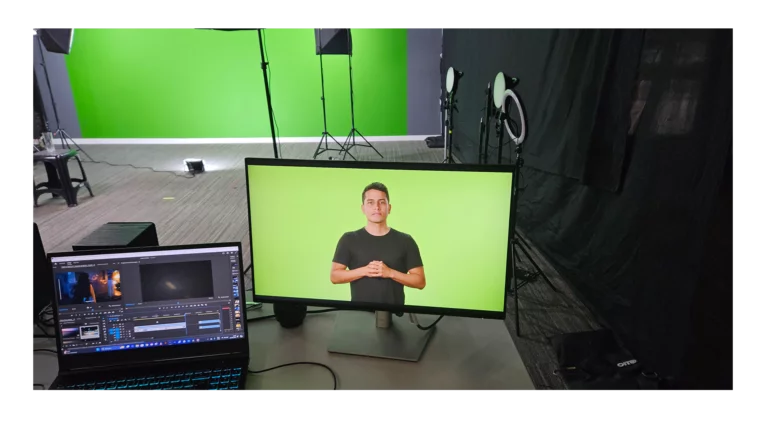Estúdio com chroma key verde, monitor exibindo gravação ao vivo, notebook com software de edição e equipamentos de iluminação